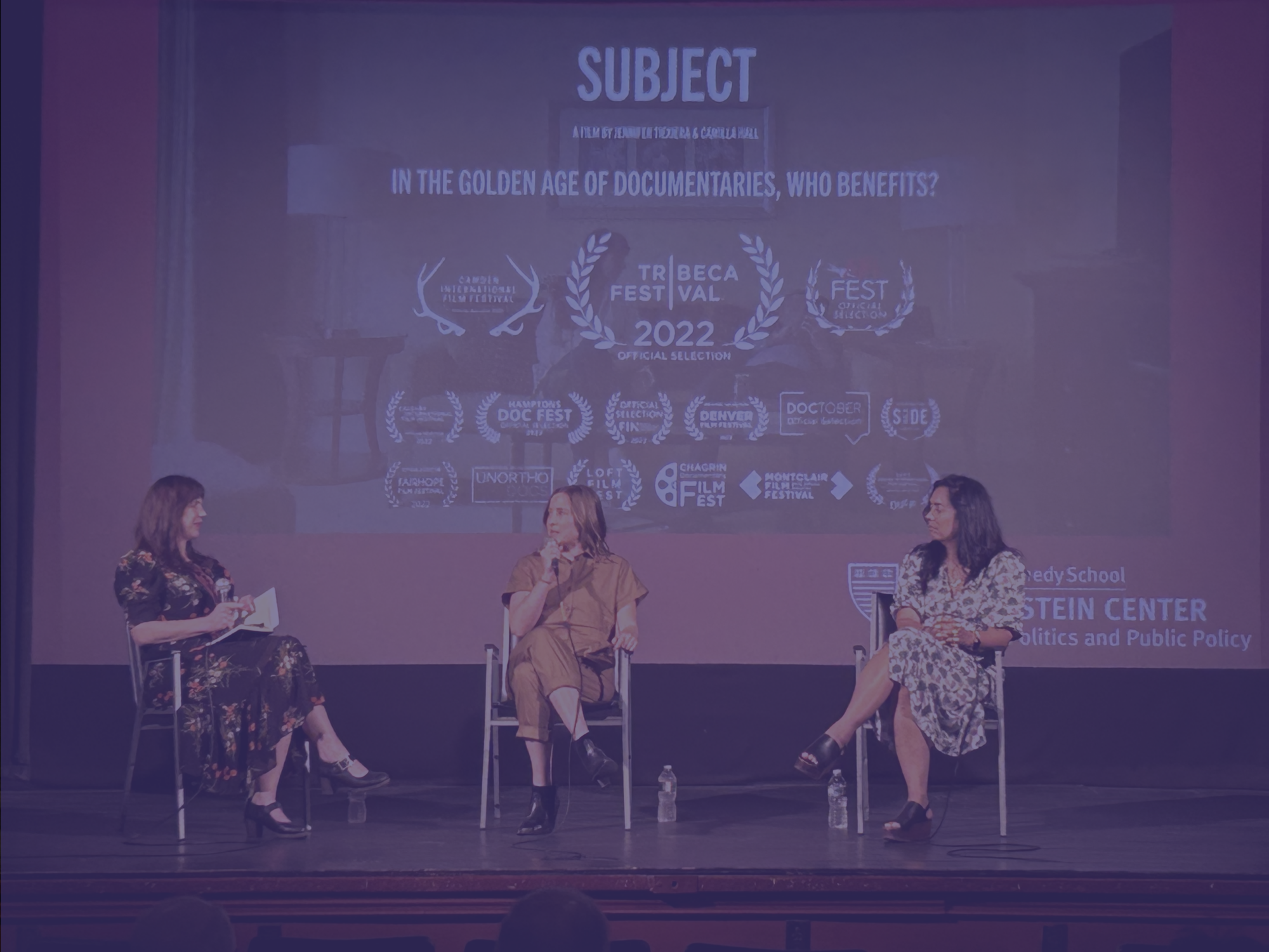 Three woman on stage seated in chairs with microphones