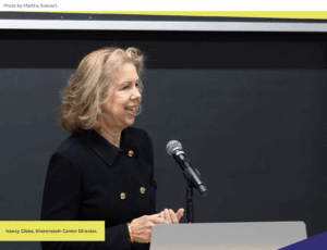 Person looking out to the right, speaking into a microphone on a podium.